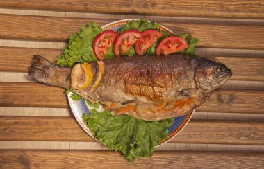 Altın kabuk ile lezzetli kızarmış balık. Limon ve domates dilimleri ile Balık salata yaprakları üzerinde bir tabak ta. üst görünüm, yakın çekim. ahşap arka plan