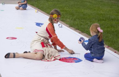 Rusya, Krasnoyarsk, Temmuz 2019: Çocuklar ve yetişkinler yerde büyük beyaz bir tuval üzerinde birlikte boya.