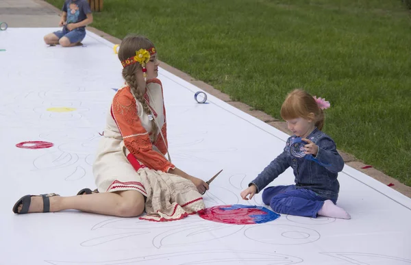 Rússia, Krasnoyarsk, julho de 2019: Crianças e adultos pintam juntos em uma grande tela branca no chão . — Fotografia de Stock