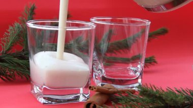 Geleneksel Noel içkisi, rendelenmiş hindistan cevizi ve tarçınlı eggnog. Kırmızı arka planda noel süslemesiyle düzenlenmiş iki bardakta eggnog kokteyli. Kokteyl bardaklara dökülüyor..