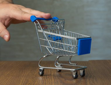 Alışveriş arabası. Arka planda, bir adam dizüstü bilgisayardan ürün sipariş ediyor. Seçici odaklanma. çevrimiçi alışveriş.