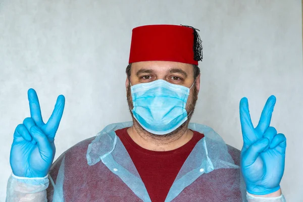 man in a medical mask and Turkish hat shows a victory sign. end of quarantine, pandemic of the coronavirus.