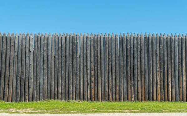 The fence is made of uncouth logs. palisade are rough and pointed to the top.