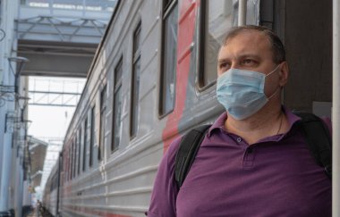 Tren vagonunun yanında maskeli bir adam var. Salgın sırasında seyahat kavramı. Koruyucu tıbbi maske takmanın kalıcı şekli. Cerrahi koruyucu maske. Tıbbi solunum bandajı yüzü.