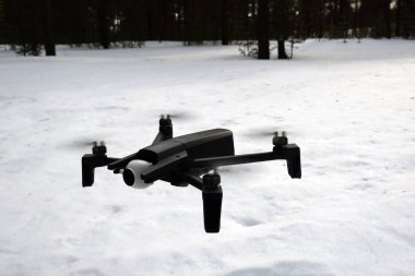 Küçük bir quadcopter kar arka planda uçar.