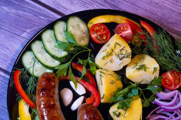 Sebze ve panoları bir arka plan ile siyah bir tabak üzerinde Güzel ızgara sosis.