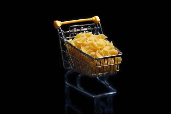 Nahaufnahme von Einkaufswagen auf schwarzem Hintergrund, Verkaufskonzept isoliert über schwarzem Hintergrund in einem Einkaufswagen liegt eine Pasta. — Stockfoto