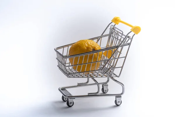 Close-up de carrinhos de compras no fundo branco. Trolley e limon, conceito de venda. Isolado sobre fundo branco em um carrinho encontra-se um citrino amarelo . — Fotografia de Stock