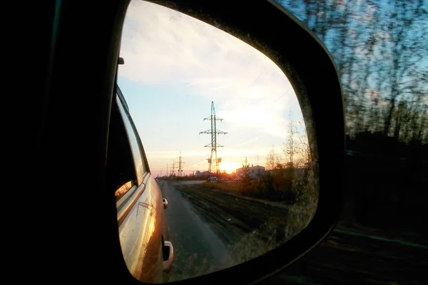 Reflektion i en bil spegel. Solnedgång och elektriskt torn på en mörk himmel bakgrund. — Stockfoto