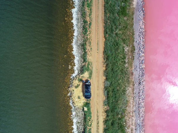The pink lake. Taken from a bird's eye view. The dark and pink lake is separated by a dirt road.