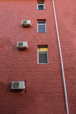 Binanın cephesi kırmızıdır. Klimalar duvara asmak, pencereler ve bir drenaj borusu vardır.