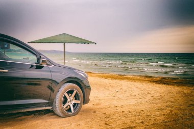 Black car stands on the seashore near the water's edge.