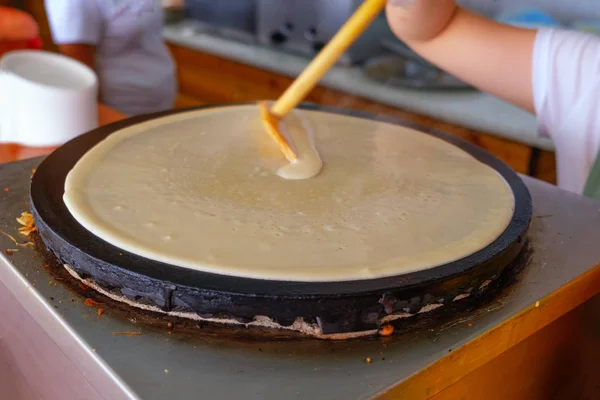 Den Prozess der Herstellung von Pfannkuchen. Der Teig breitet sich auf der Herdplatte aus. Selektiver Fokus. lizenzfreie Stockfotos