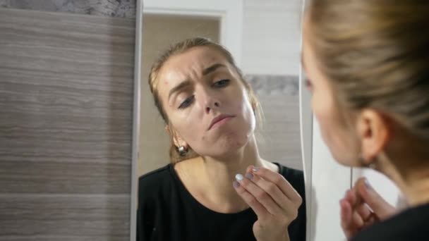 Fille avec de l'acné sur le visage est une salle de bain par le miroir — Video