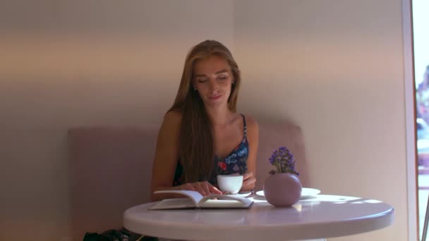 Fille dans un café feuilletant un livre — Video