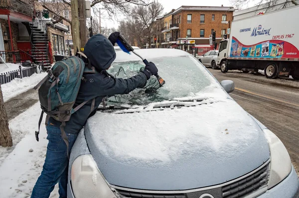 Montreal, Canada - 7 February 2019: man cleaning car windshield from ice with scraper tool.