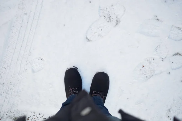 一名男子穿着一双黑色靴子站在被雪覆盖的地面上 地面上有几块脚印 这是一个自上而下的镜头 — 图库照片