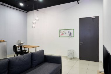 Bir stüdyo daireküçük bir oturma odasında siyah bir kanepe. Arka planda küçük bir yemek masası. Bazı dekoratif öğeleri ile boş bir beyaz duvar.