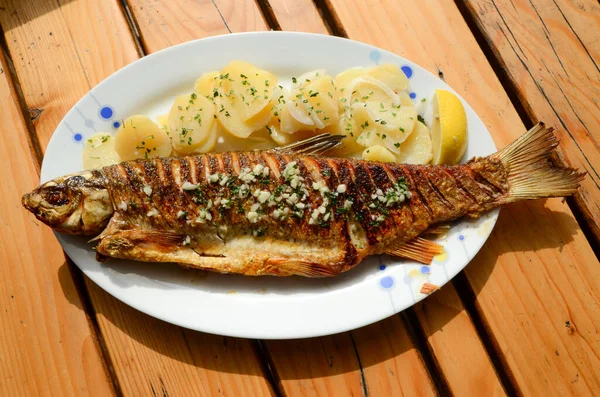 Grilled fresh fish in restaurant. Tasty and delicious fish with potatoes, lemon and garlic on plate on wooden table