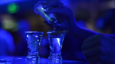 Mavi gece kulübü ışıklarıyla barda tekila bardaklı kişinin kısmi görüntüsü 
