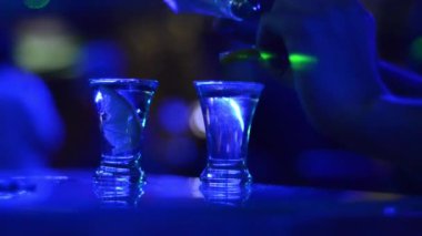 Mavi gece kulübü ışıklarıyla barda tekila bardaklı kişinin kısmi görüntüsü 