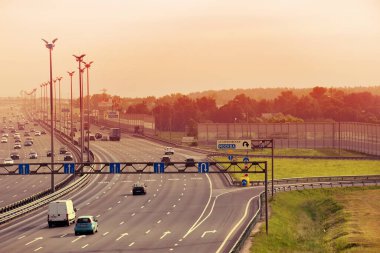 Güneşli bir sabahta şehir otoyolunda arabalar hızlı gider.