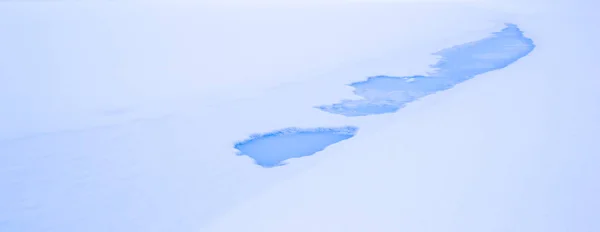 Blue thaw patches in ice and snow on a winter lake