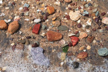 Biraz köpük üzerinde deniz suyu ile sahil kenarına renkli küçük taşlar