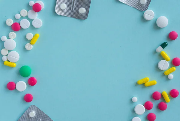 Blisters with tablets and capsules, multi-colored tablets Scattered around: white, pink, yellow, green. Medical concept on a blue background, pharmacy. Copy space for text in the center of the photo.