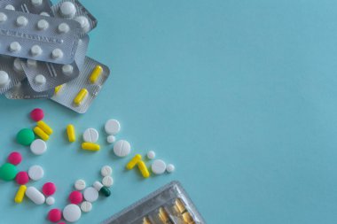 Fotoğrafın sol tarafında mavi arka planda farklı şekillerde ve renklerde haplar var. Tıbbi konsept, sağdaki metin için yer. Uzayı kopyala Eczane, kendine dikkat et..