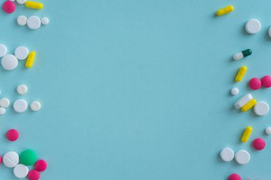 Tabletlerin farklı şekilleri ve renkleri sol ve sağ tarafında kaotik bir şekilde duruyor. Mavi arka planda tıbbi konsept, eczane. Metin için boş alan. Boşluğu kopyala