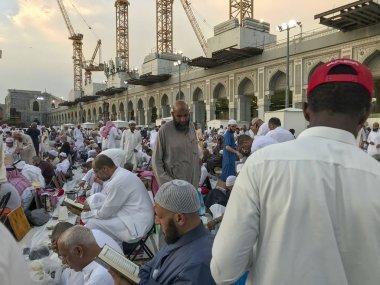 Mekke, Suudi Arabistan-Circa Haziran 2019: Kimliği belirsiz Müslüman erkekler Ramazan ayında Mescid-i Haram içinde oruç beklerken Kur'an-ı Kerim okuyup namaz kılıyor.