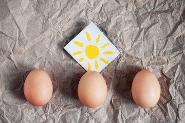 Üç kahverengi yumurta ve hayat sembolü ve baharın başlangıcı olarak bir ışık parşömen arka plan üzerinde güneşin. Paskalya kavramı