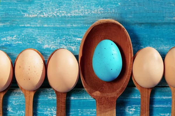 Easter eggs in wooden spoons on a blue wooden background