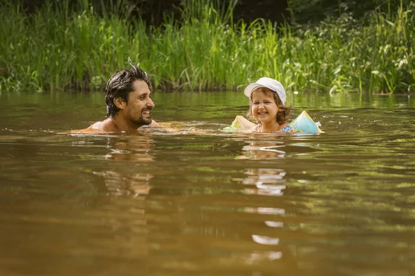 Padre e hija se bañan en el río y ríen, niño en mangas inflables para mayor seguridad — Foto de Stock