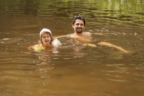 Padre e hija se bañan en el río y ríen, niño en mangas inflables para mayor seguridad — Foto de Stock
