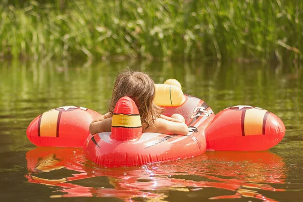 Lycklig liten flicka som leker i Uppblåsbara röda planein vatten på varm sommardag. Barnen lär sig att simma. Barn vatten leksaker — Stockfoto