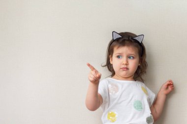 Küçük kız çocuk beyaz bir tişört içinde yan, bej renkli arka plan, yakın çekim, portre, copyspase için onun parmağını gösterir