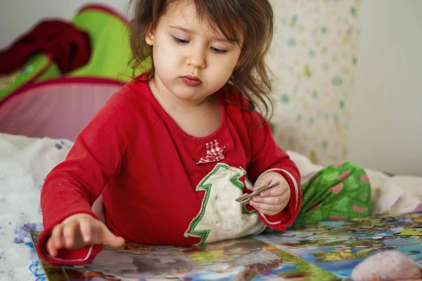 little girl Caucasian appearance in pajamas collects puzzles in a room