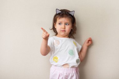 Küçük kız çocuk beyaz bir tişört içinde yan, bej renkli arka plan, yakın çekim, portre, copyspase için onun parmağını gösterir