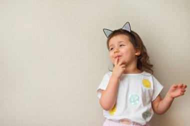 Küçük kız sinsice görünüyor ve sinsice tarafına, parmaklarını dokunmatik onun dudakları, yakın çekim, bej renkli arka plan, gün, copyspase