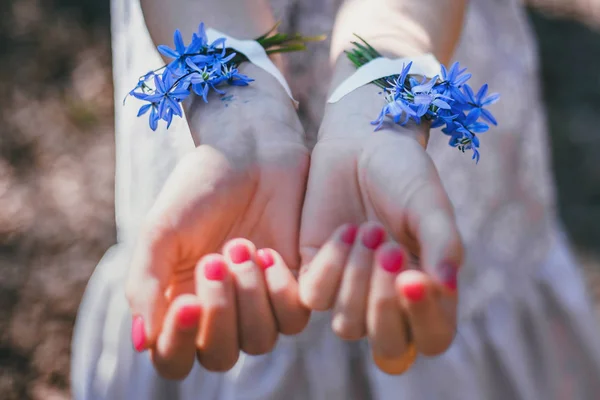 Blue snowdrops glued to girlish young hands with a bright manicure, day, close-up. Concept - love of nature, creative art