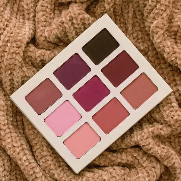 Palette of cosmetic shadows for everyday makeup on textured fabric sweater, close-up, flatlay