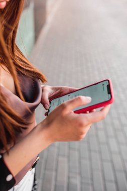 Mutlu genç kız, güneşli bir günde sokakta yürürken akıllı telefon kullanıyor.