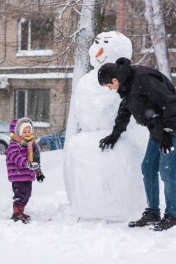 Baba ve küçük bir çocuk sokakta birlikte vakit geçiriyorlar, kar fırtınasında bir kardan adam heykeli yapıyorlar..