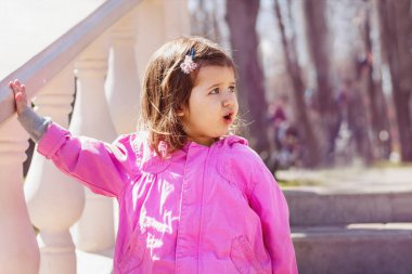 Pembe ceketli küçük kız eğlence parkında yüzünü çeviriyor. Gözleri ve ağzı sonuna kadar açık, sürprize şaşırıyor..