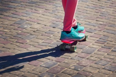 Pembe tayt ve mavi spor ayakkabı giyen genç kaykaycı bacakları.