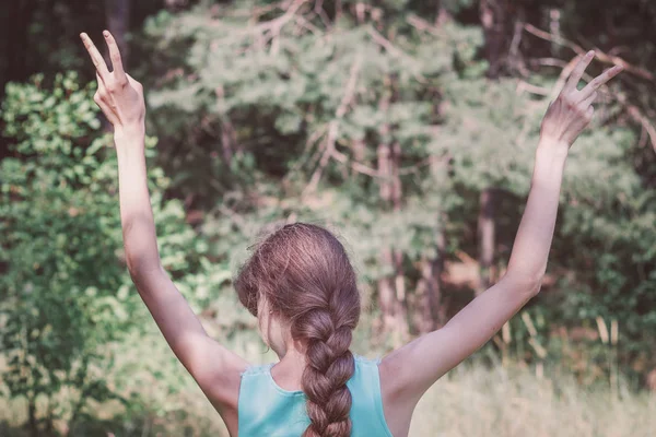 Vista posteriore di una ragazza con i capelli lunghi in una treccia, puntando due dita verso l'alto gesto, spazio libero. Libertà, tranquillità concetto di benessere . — Foto Stock