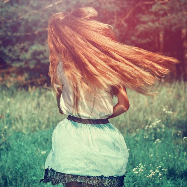 Una adolescente con una falda y una blusa blanca salta, agitando el pelo largo y rubio al aire libre, en un tono de moda — Foto de Stock