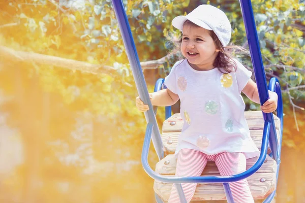 Little baby girl caucasian appearance sitting on a swing and laughing